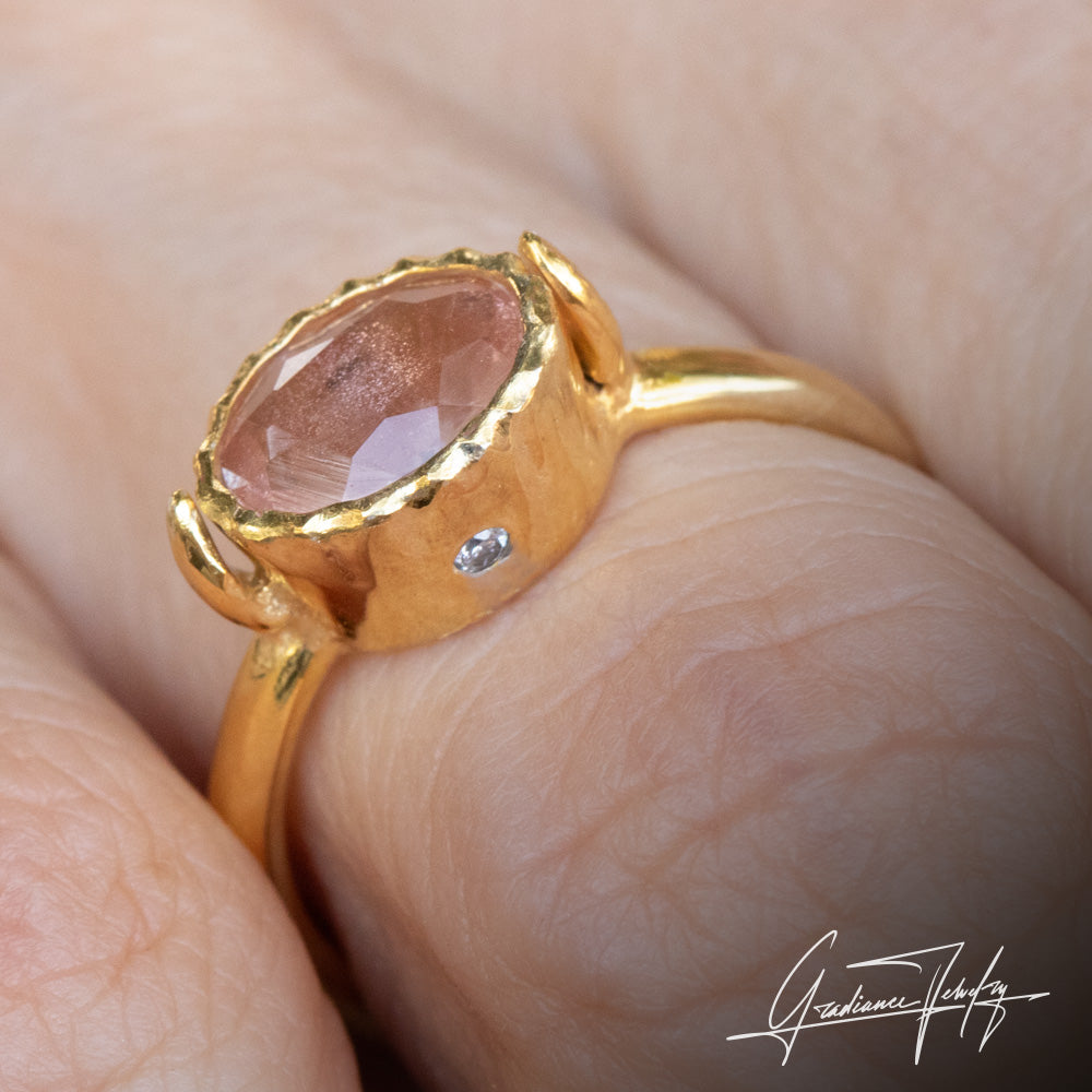 Gradiance Jewelry Sun Chaser Collection: women's 14KT yellow gold Rose ring featuring an oval Oregon Sunstone with schiller effect, accented by two diamonds and a leaf design, displayed on a finger with side view.